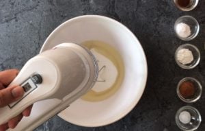 electric mixer whisking oil and sugar in bowl