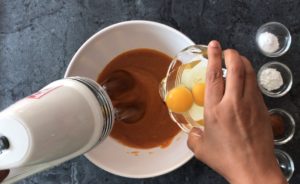 hand pouring eggs into bowl with pumpkin mixture