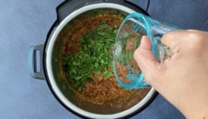 pouring water into instant pot with herbs, ground meat and tomatoes