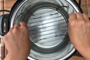 two hands placing trivet in instant pot with water