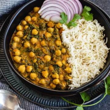 chana saag and cumin rice with sliced red onions in black bowl