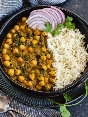 chana saag and cumin rice with sliced red onions in black bowl