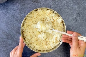 two hands fluffing rice with fork