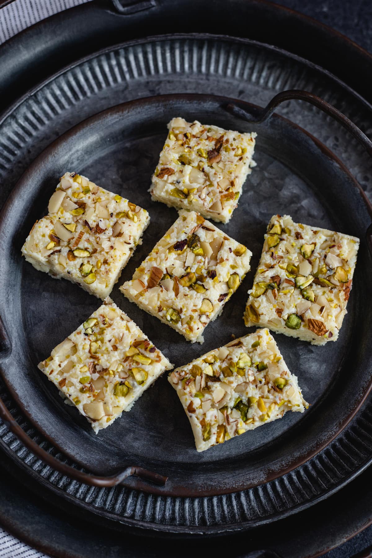 kalakand squares topped with pistachios and almonds on black plate