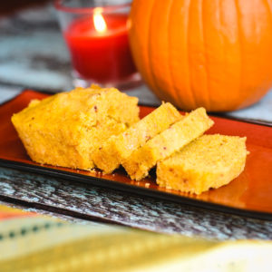 sliced pumpkin cornbread loaf on platter with pumpkin in background