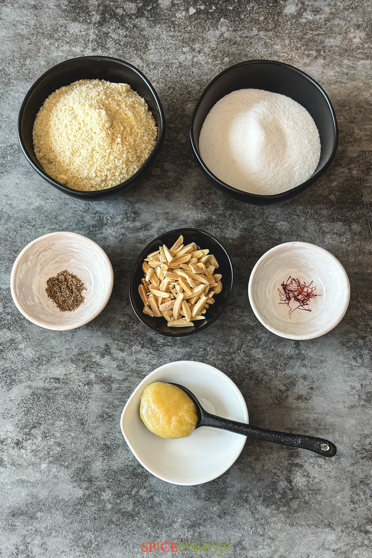 Almond flour, sugar, cardamom among other ingredients in bowls on grey board