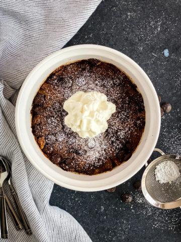 Chocolate bread pudding in a white bowl topped with whipped cream