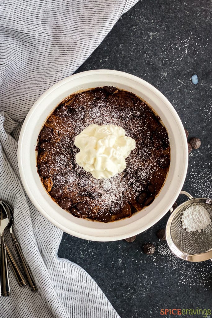 Chocolate bread pudding in a white bowl topped with whipped cream