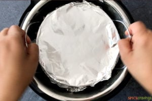 Two hands placing tin foil inside an Instant Pot
