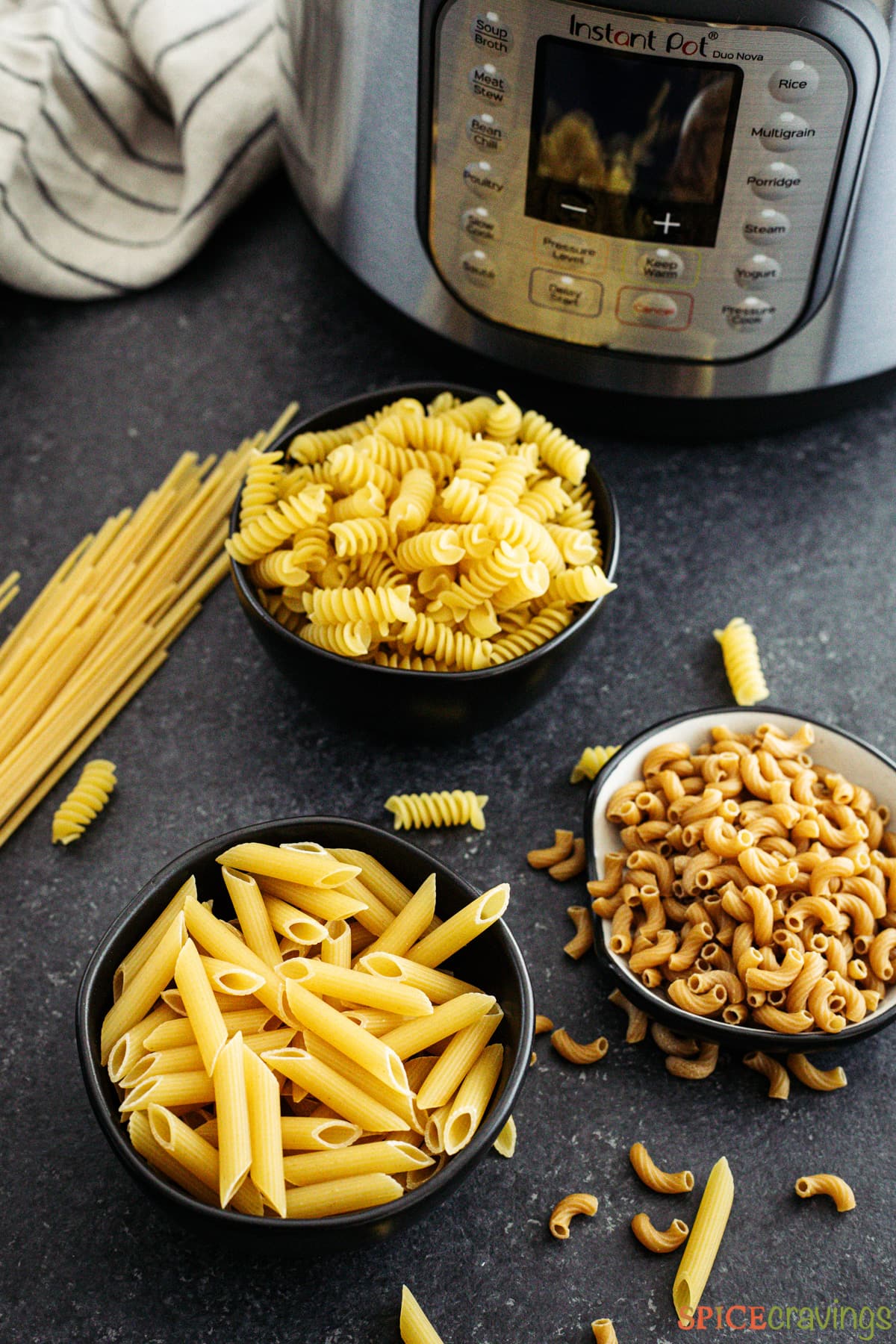 Three bowls of uncooked pasta next to an Instant Pot