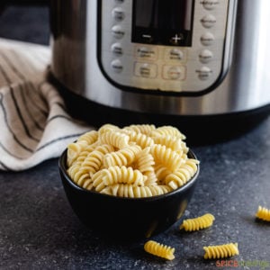 A bowl of cooked rotini pasta next to an instant pot
