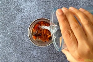 A hand pouring ingredients for sauce into a mason jar
