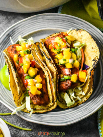 Two grilled fish tacos topped with mango salsa