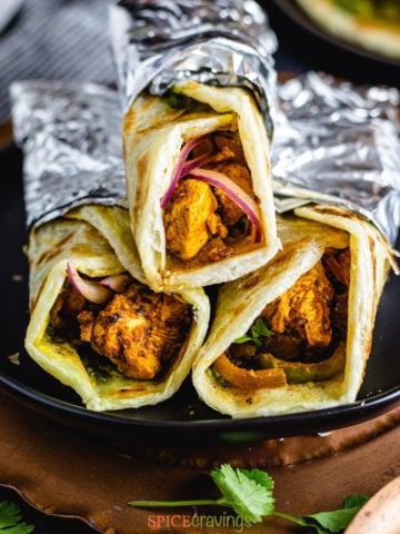 Chicken kathi rolls wrapped in aluminum foil on a plate