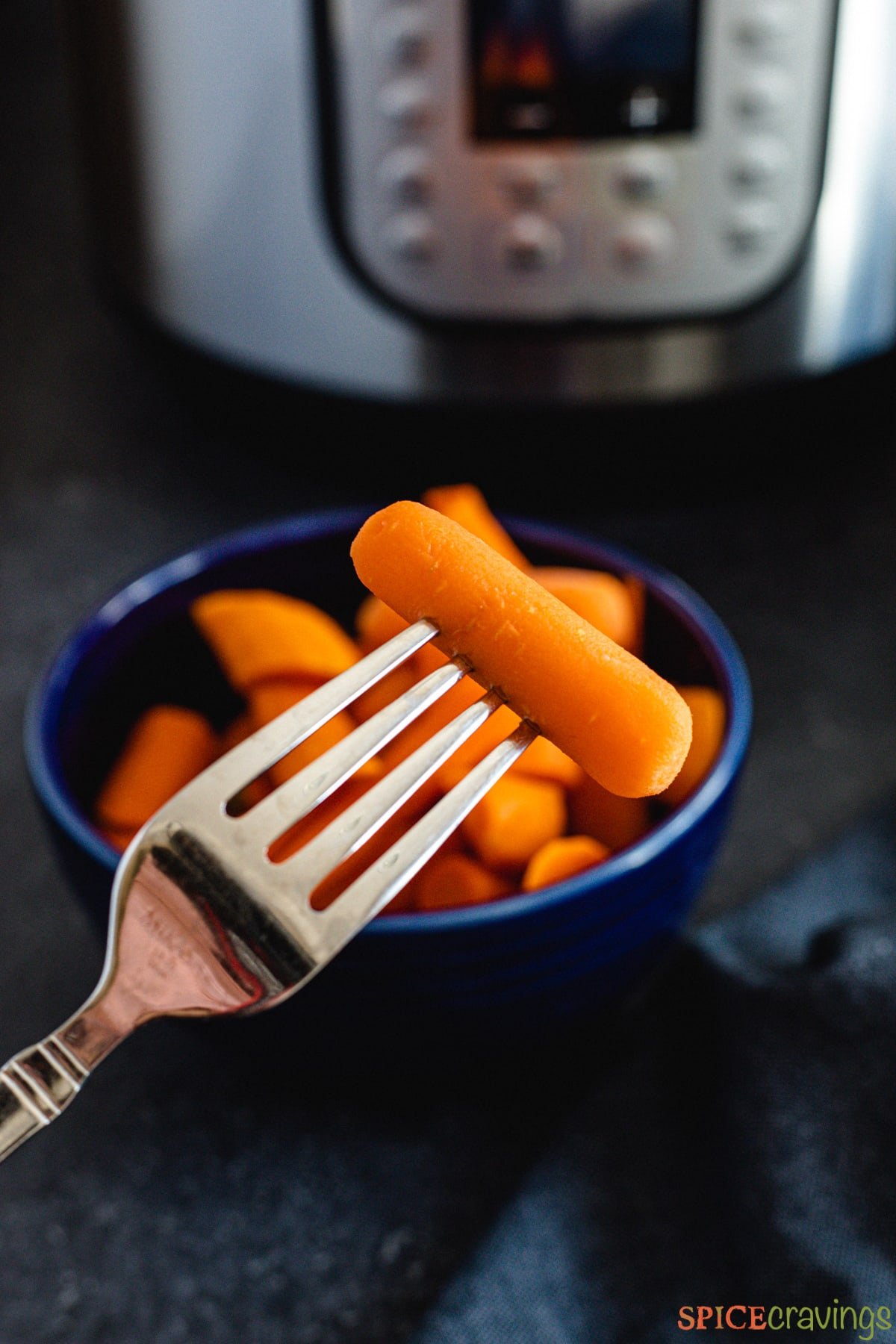 A fork lifting a carrot from a bowl with an Instant Pot in the background