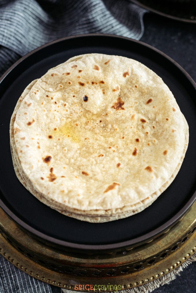 Cooked Roti brushed with ghee and stacked on a black plate