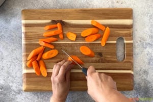 Carrots being cut on a wooden cutting board