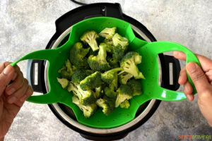Broccoli in a steamer basket being lowered into a pressure cooker