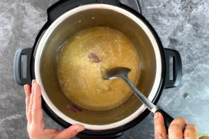 A spoon stirring liquid inside of a pressure cooker