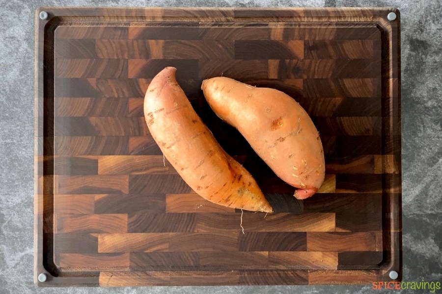 Two unpeeled sweet potatoes on a cutting board