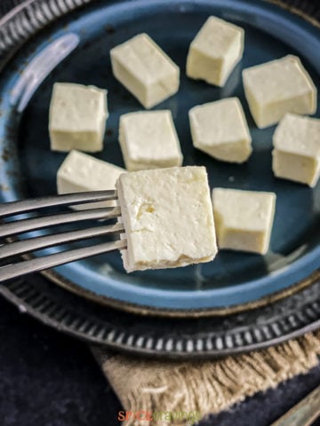 Paneer cubes on a black plate with a fork piercing a cube