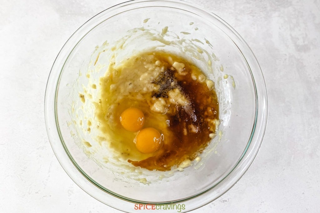 two eggs, vanilla extract, maple syrup and mashed bananas in glass bowl
