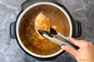 Lifting chicken out of a pressure cooker with tongs