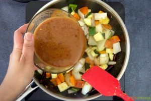 Pouring Kung Pao sauce into a skillet with vegetables
