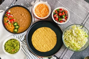 Plate of tostada surrounded by beans, cheese, guacamole, salsa, lettuce