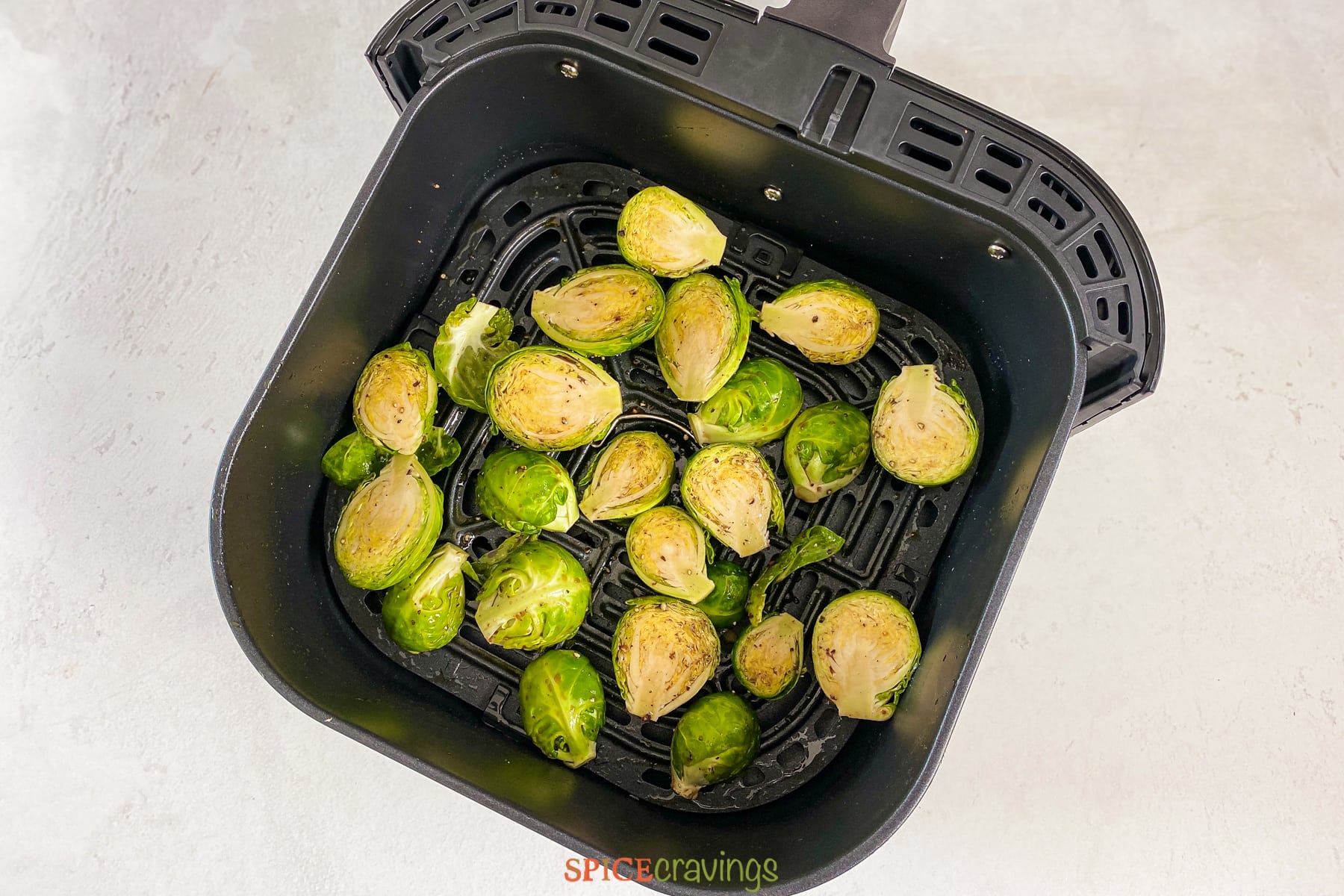Seasoned brussel sprouts spread in air fryer basket, ready to cook