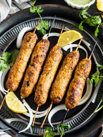 5 skewers of chicken kebab on metal plates with cilantro and onion