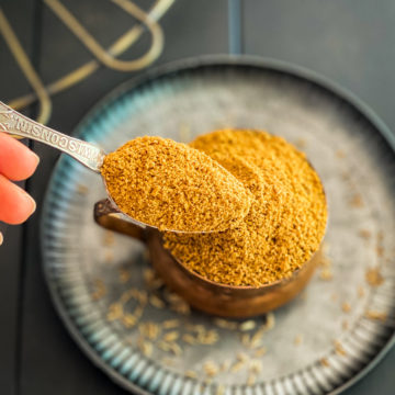 hand scooping spoonful of cumin powder in bowl