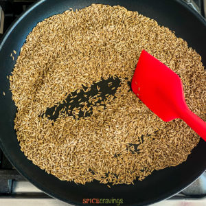 cumin seeds in skillet with red spatula