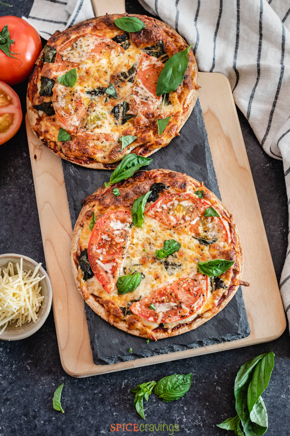 Two pizzas with tomato and basil on a slate board