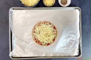 Flatbread topped with sauce and cheese on baking tray