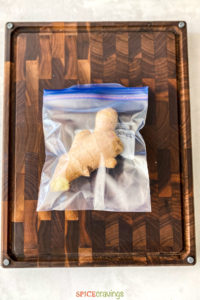 unpeeled ginger root in plastic storage bag on wooden cutting board