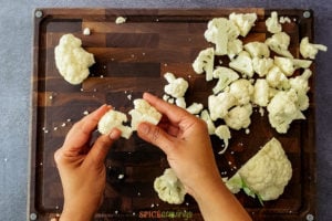 two hands breaking cauliflower into florets