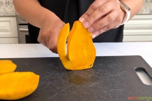 two hands slicing small cheek off mango
