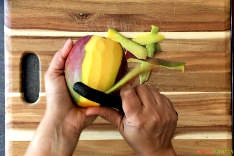 two hands peeling mango with vegetable peeler