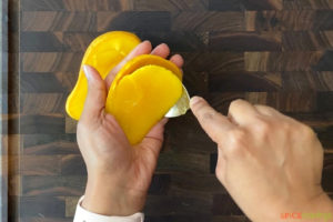two hands scooping out mango flesh with a spoon