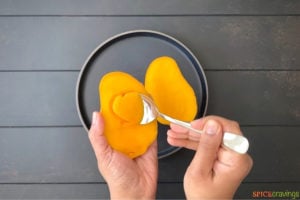 two hands scooping mango flesh with a spoon