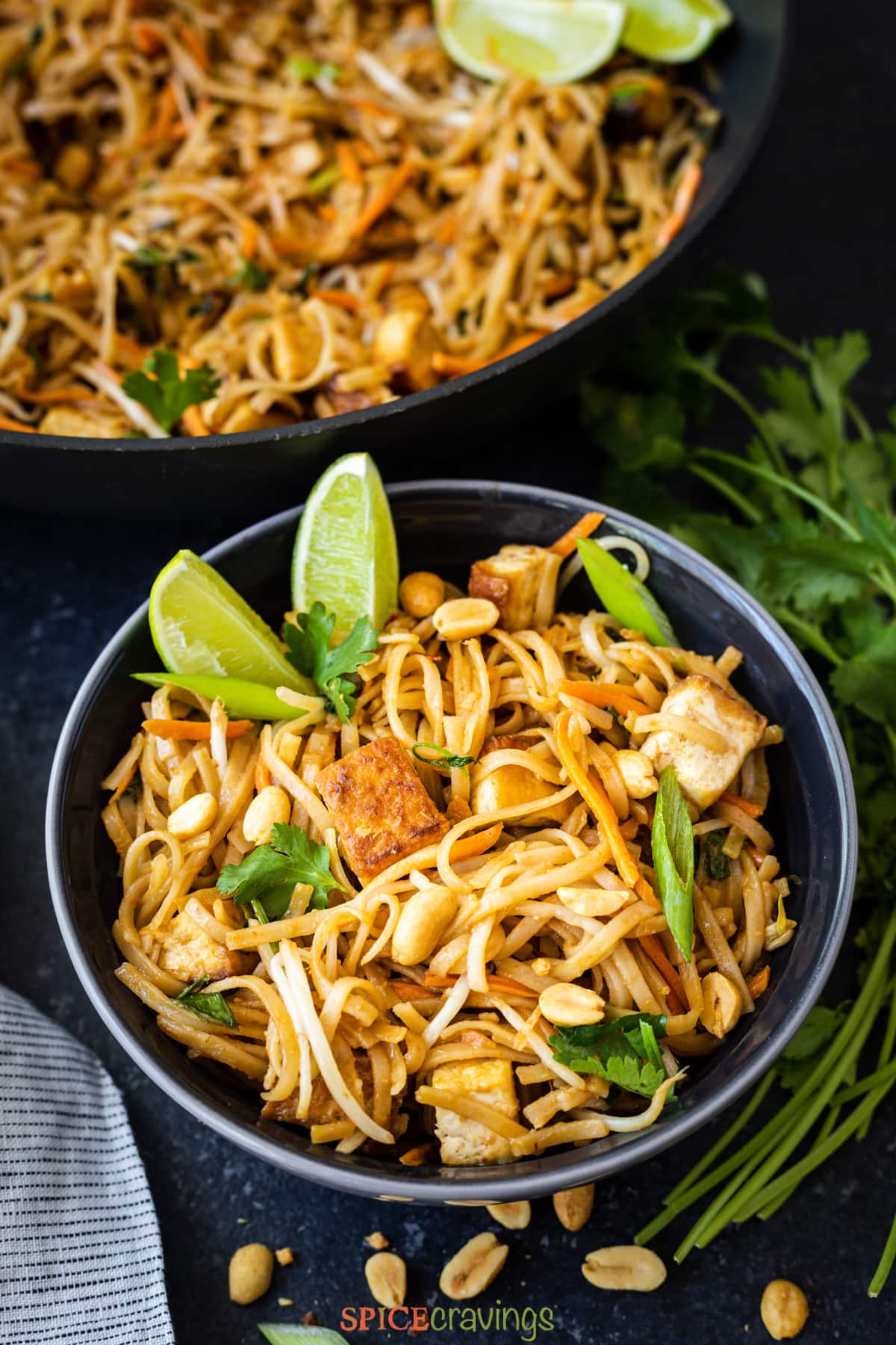 pad thai with tofu and lime wedges in black bowl
