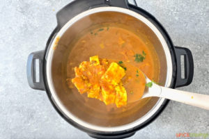 paneer cubes scooped out of instant pot of butter masala with ladle