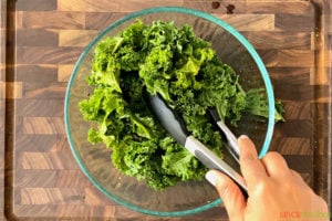 Tossing kale leaves in bowl using tongs