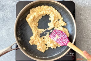 Sauteing ladoo dough in skillet with purple spatula