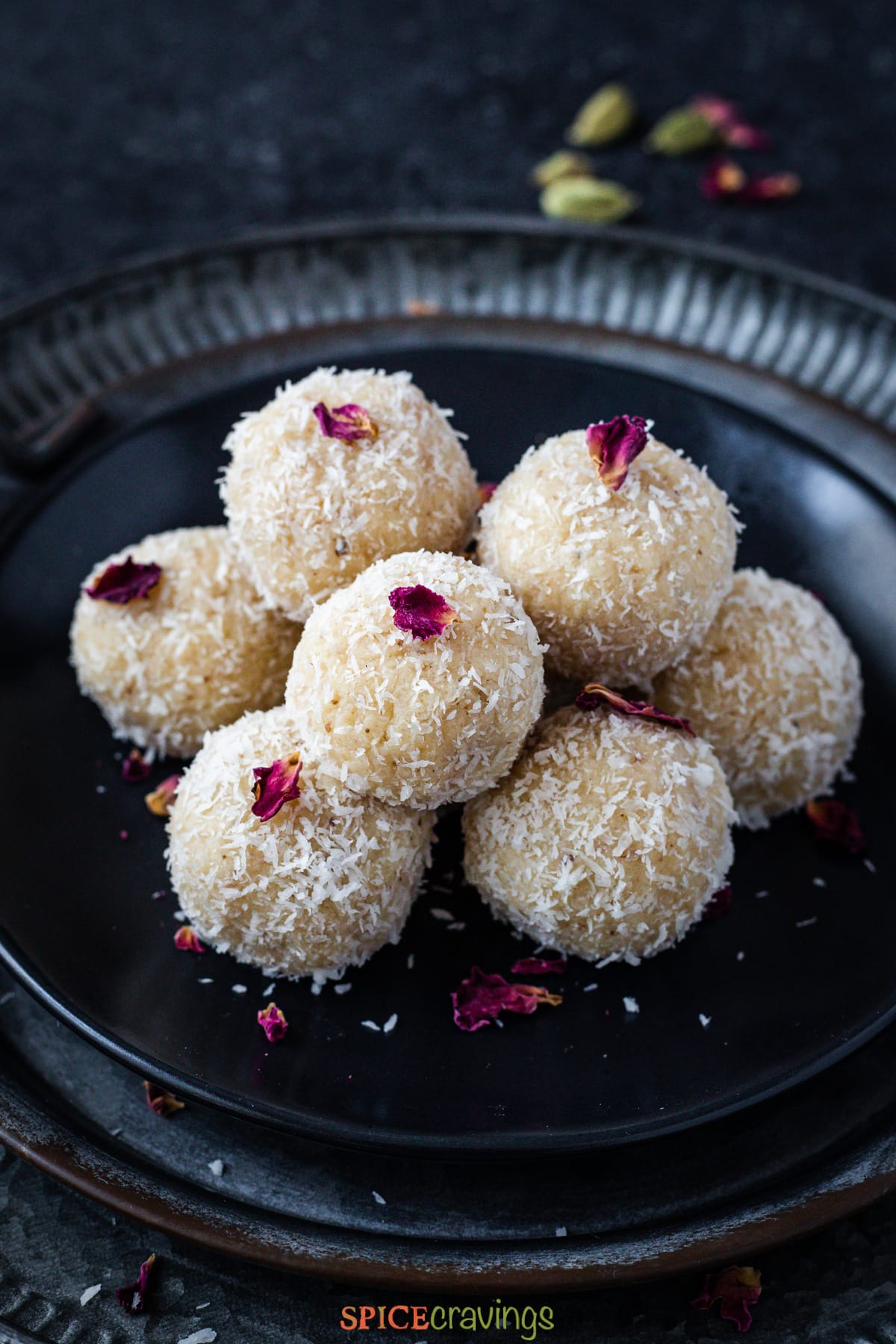 stacked coconut laddu topped with dried rose petal on metal plate