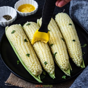 four pieces of corn on the cob on a plate being brushed with butter
