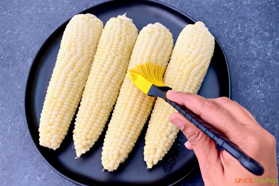 corn cobs being brushed with butter