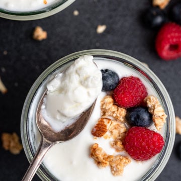 Spoon full of yogurt from a cup topped with granola and berries