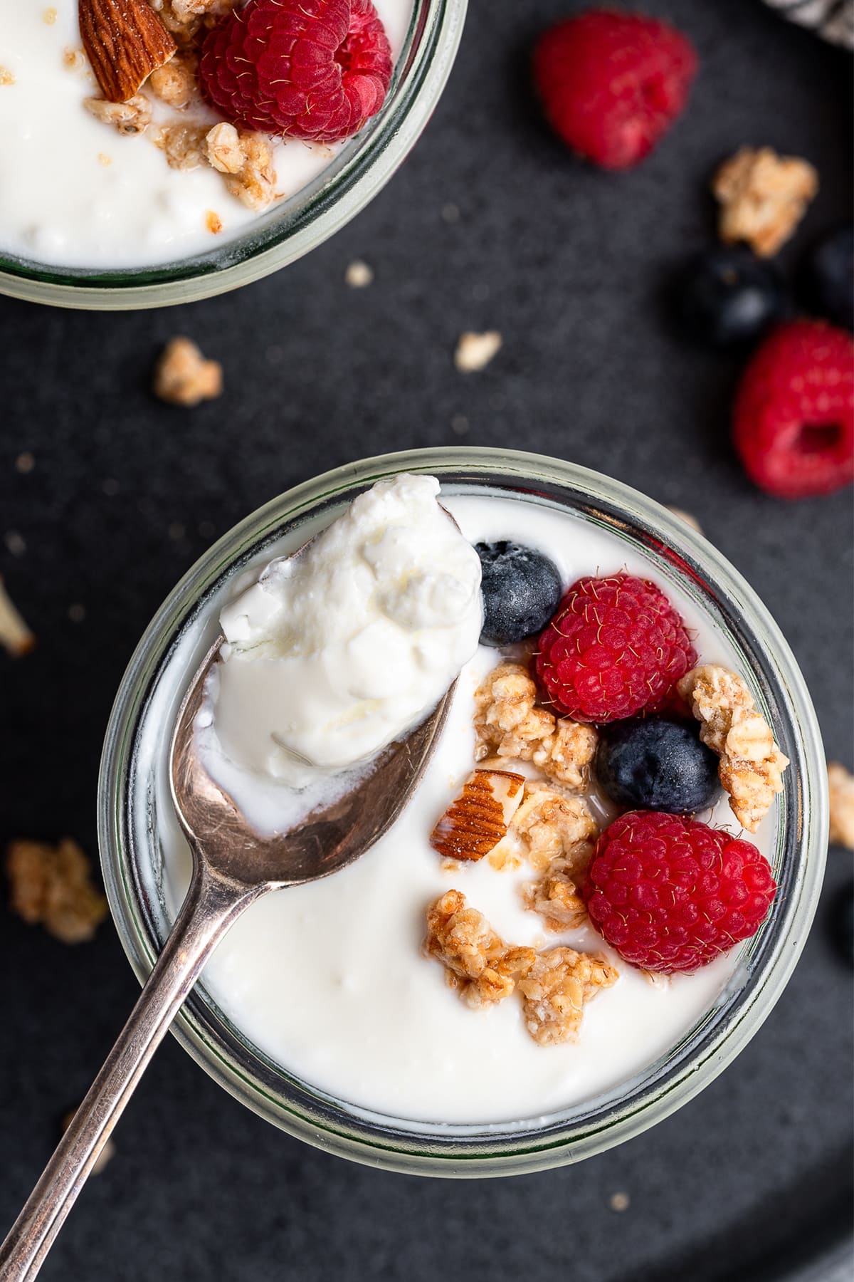 Spoon full of yogurt from a cup topped with granola and berries